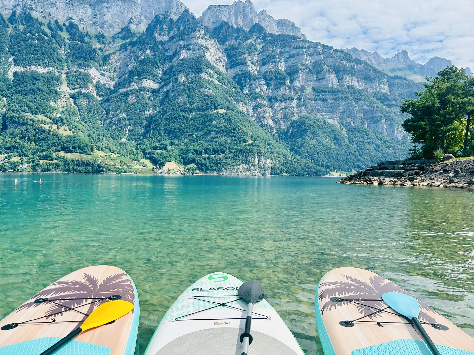 Drei SUP-Boards mit Paddeln auf dem spiegelglatten, türkisen Wasser unterhalb der Churfirsten-Felswände